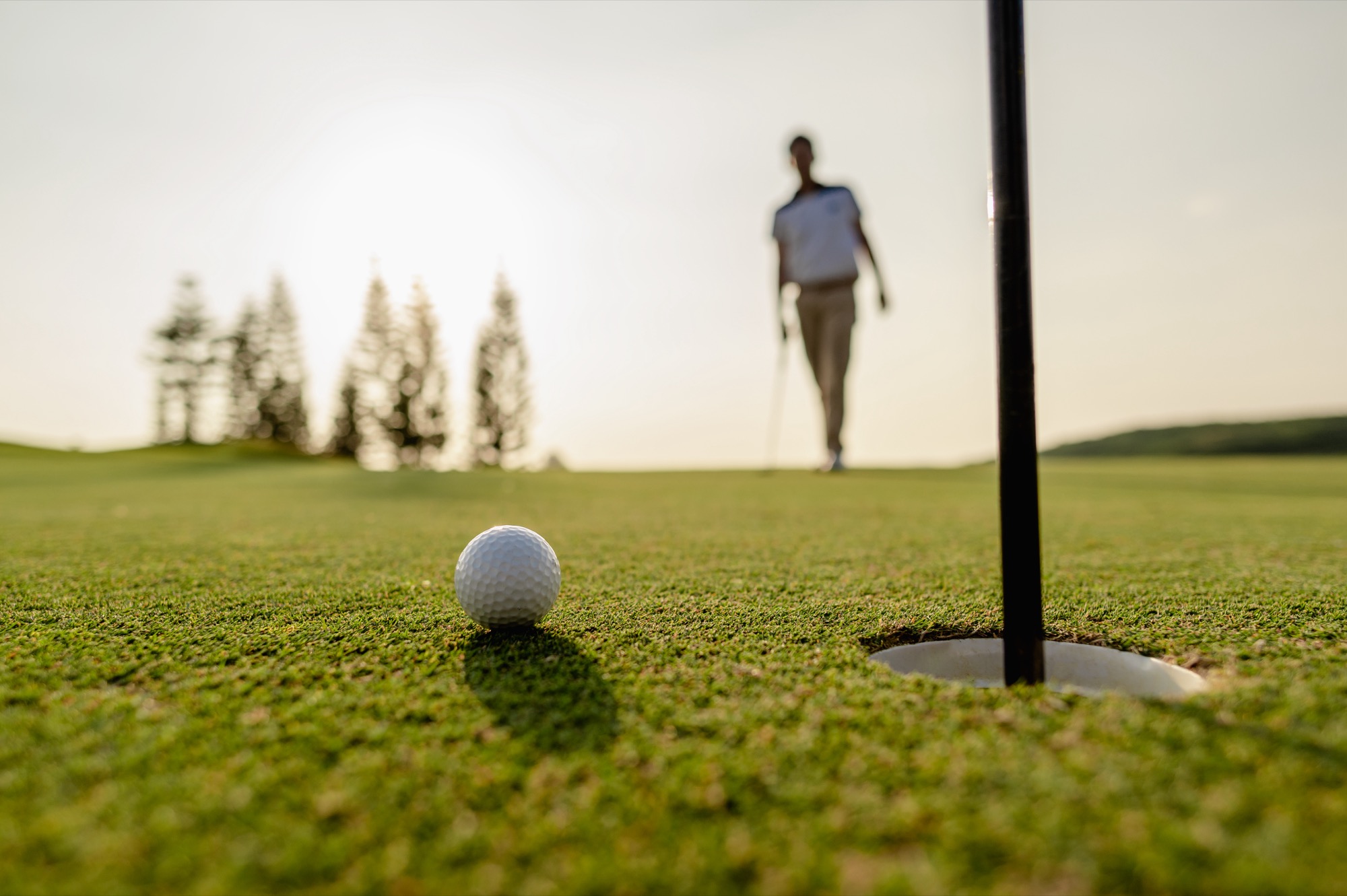 Golf ball resting on the edge of the hole at sunset